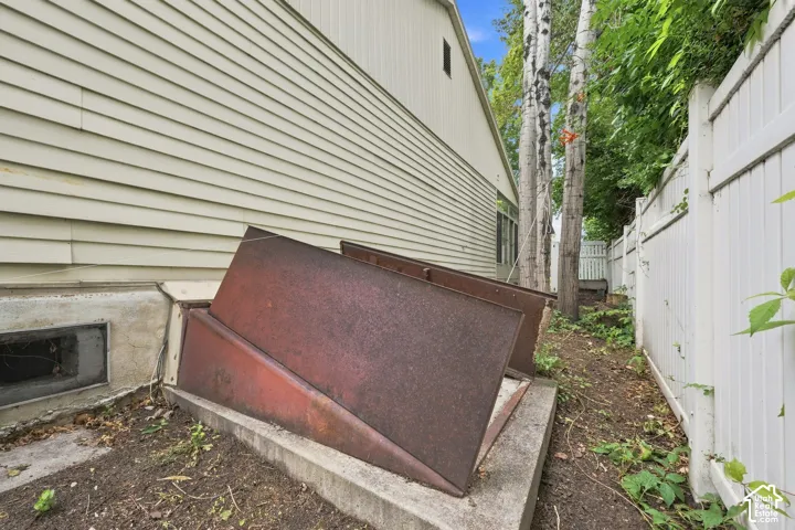 Siding exterior with a concrete foundation, a basement access, and a perimeter fence