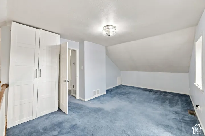 Sloped ceilings with a flush-mount light fixture, blue carpeting, and built-in white paneled wardrobes
