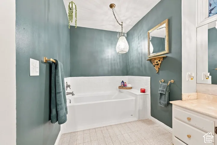 White Soaker bathtub with subway tile surround, vanity with a light-toned countertop, and an overhead chandelier