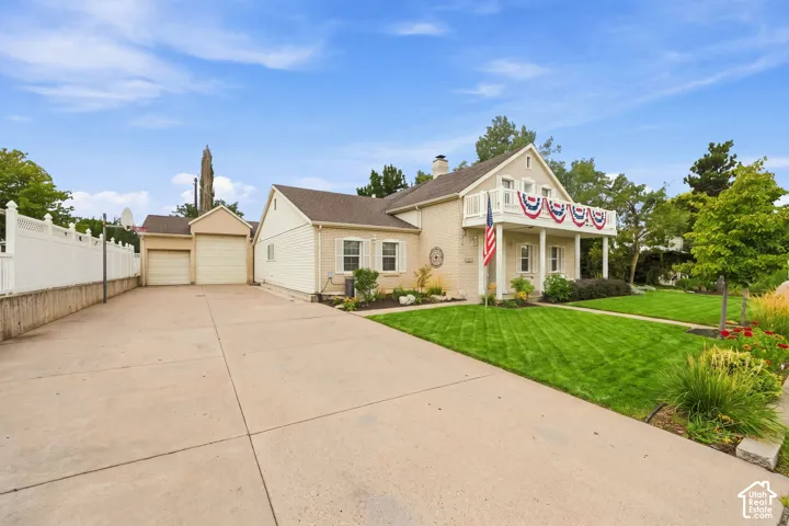 Charming residence featuring a spacious concrete driveway with two-car garage, manicured lawn with mature landscaping, and patriotic front entry d