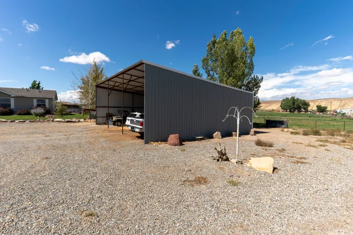 Metal-frame carport with a corrugated metal roof and siding, situated on a gravel lot