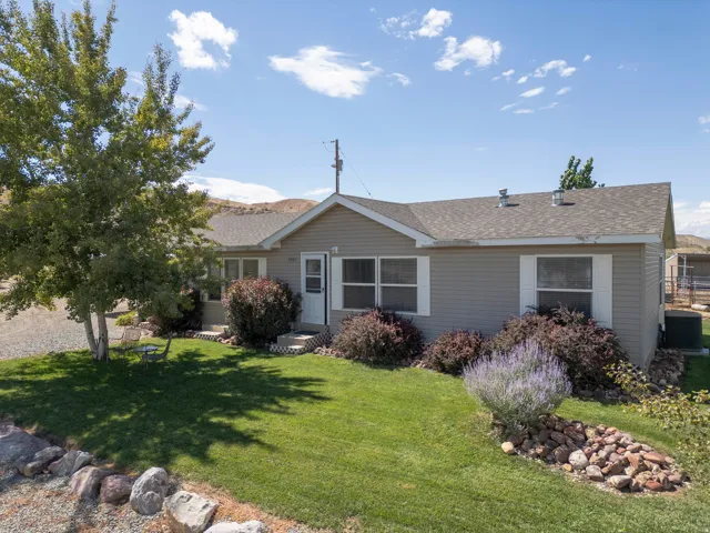 Charming single-story home with a manicured front lawn, mature landscaping featuring ornamental shrubs and ground-level rock borders, and a gabled roofline with updated siding