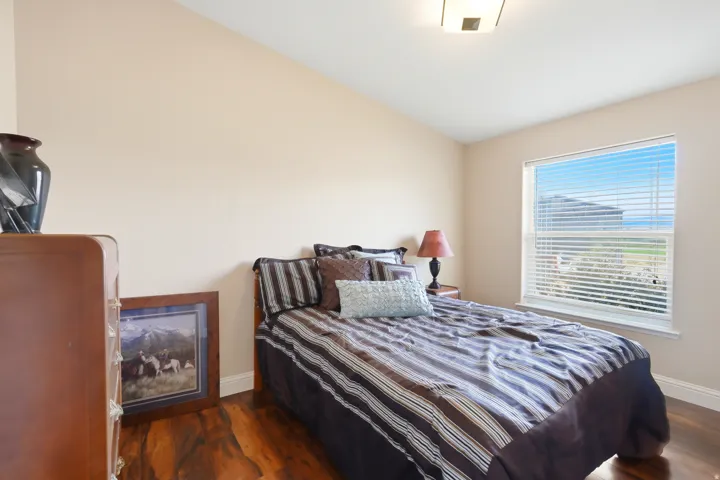 Bright secondary bedroom showcasing wood-finish flooring, large windows with plantation shutters, and soft neutral wall finishes