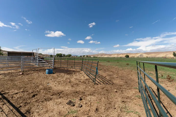 Metal fencing enclosing a dirt pen, with a covered structure in the background