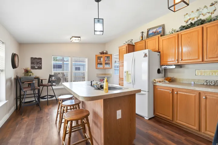 Kitchen featuring wood-finish flooring, light wood cabinetry, white appliances, a center island with an integrated sink, and recessed lighting