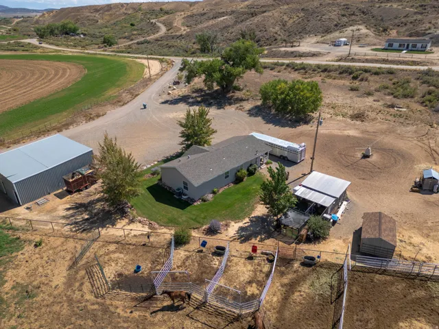 Single-story residence with a gray shingled roof, accompanied by a metal-sided utility building, multiple fenced animal pens, and a gravel driveway