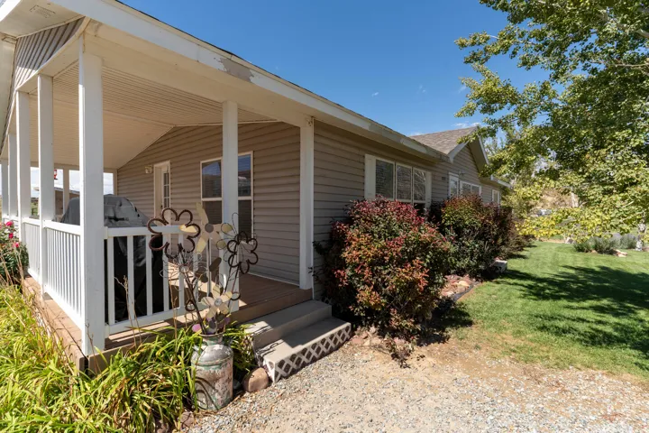Covered porch with white railings and columns, siding exterior, mature shrubs, and a well-maintained lawn