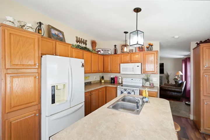 Kitchen featuring wood-finish cabinetry, a central island with an integrated sink, white appliances, and pendant lighting
