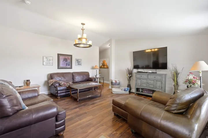 Spacious living area featuring wood-finish flooring, a contemporary chandelier, and light-colored walls
