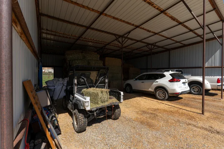 Open-air metal shed with a corrugated roof and gravel flooring, providing covered space