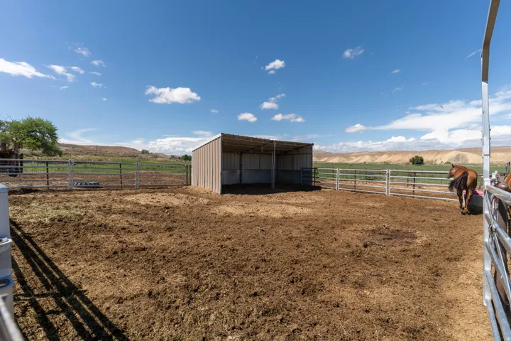 Enclosed paddock area featuring metal fencing, a covered shelter, and expansive open-air space