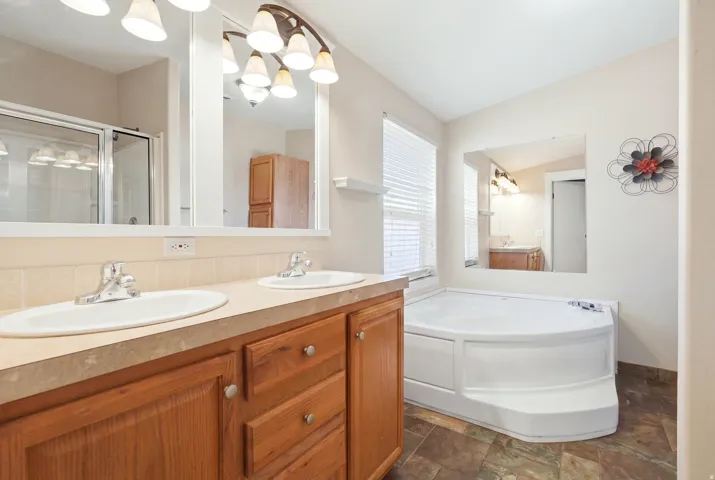 Dual vanity with wood-finish cabinetry, a large built-in mirror, a corner soaking tub, and a separate glass-enclosed shower