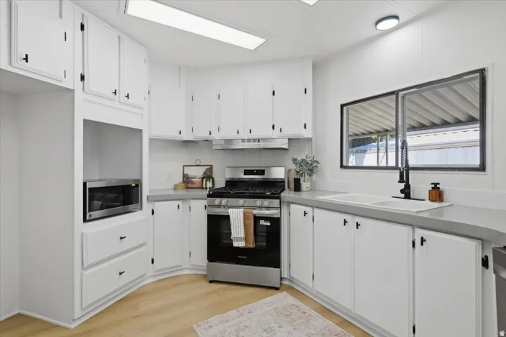 Kitchen featuring white cabinetry, light-toned countertops, a stainless steel range, and wood-finish flooring
