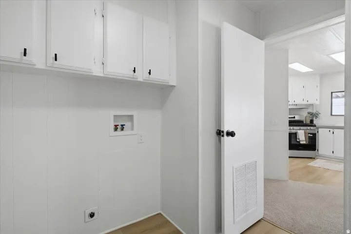 Utility space featuring white cabinetry with black hardware, wood-finish flooring, and wall paneling
