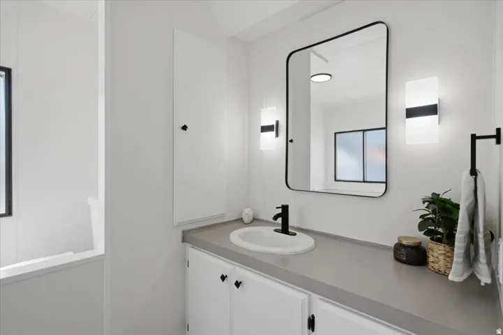 Vanity with a single basin, wall-mounted sconces, and a framed mirror