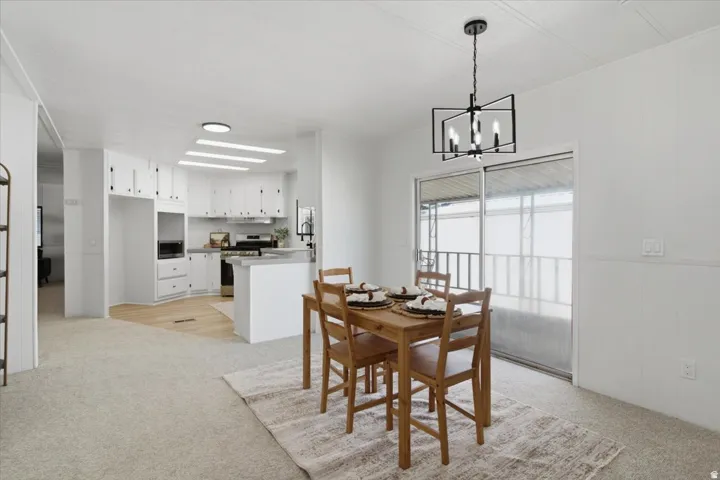 Open-concept dining and kitchen area with light-toned carpeting and wood-finish flooring