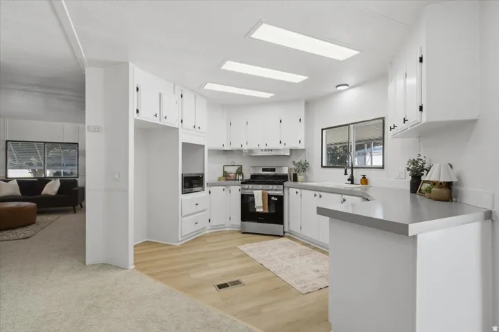 Kitchen with white cabinetry, light countertops, stainless steel appliances, wood-finish flooring, and recessed lighting