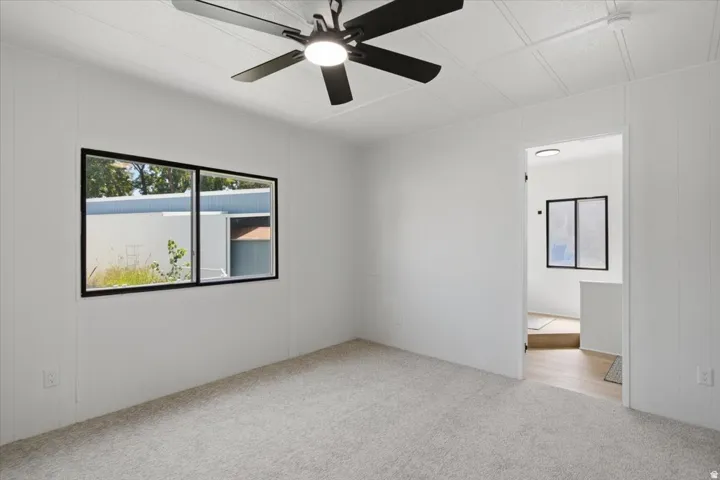 Recessed lighting, light-toned carpeting, ceiling fan with integrated lighting, white paneled walls, and black-framed window