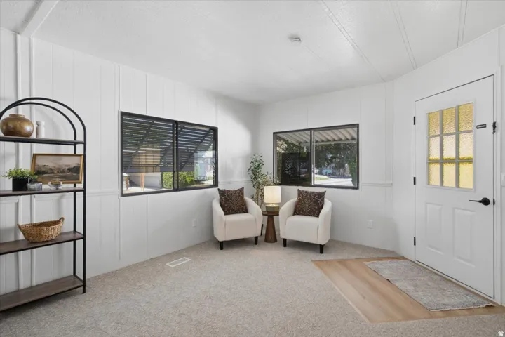 White paneled walls with wainscoting, black-framed windows, textured glass entry door, and wood-finish flooring at entry
