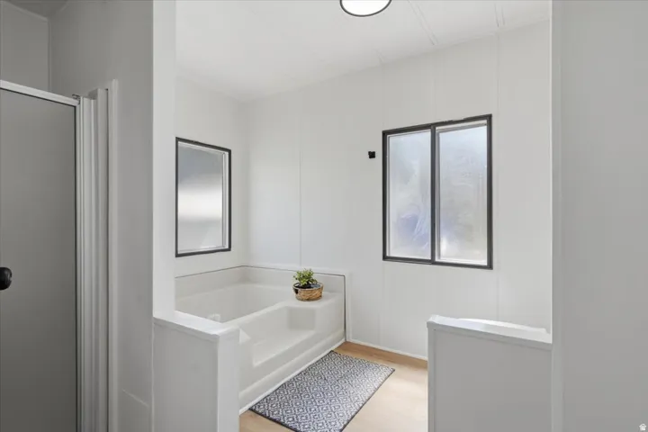 Built-in soaking tub with steps, light wood-finish flooring, and two frosted pane windows with black frames