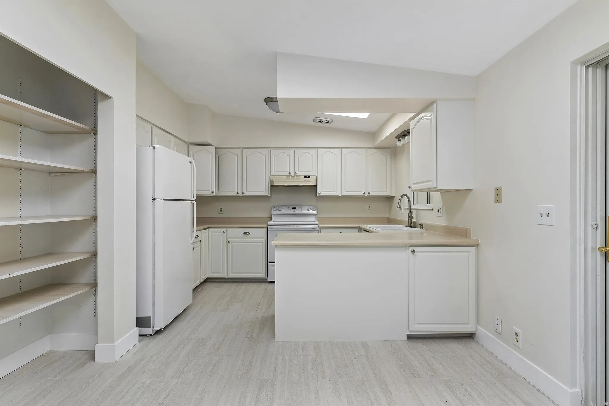 Kitchen featuring white cabinetry, light-toned countertops, white appliances, and wood-finish flooring