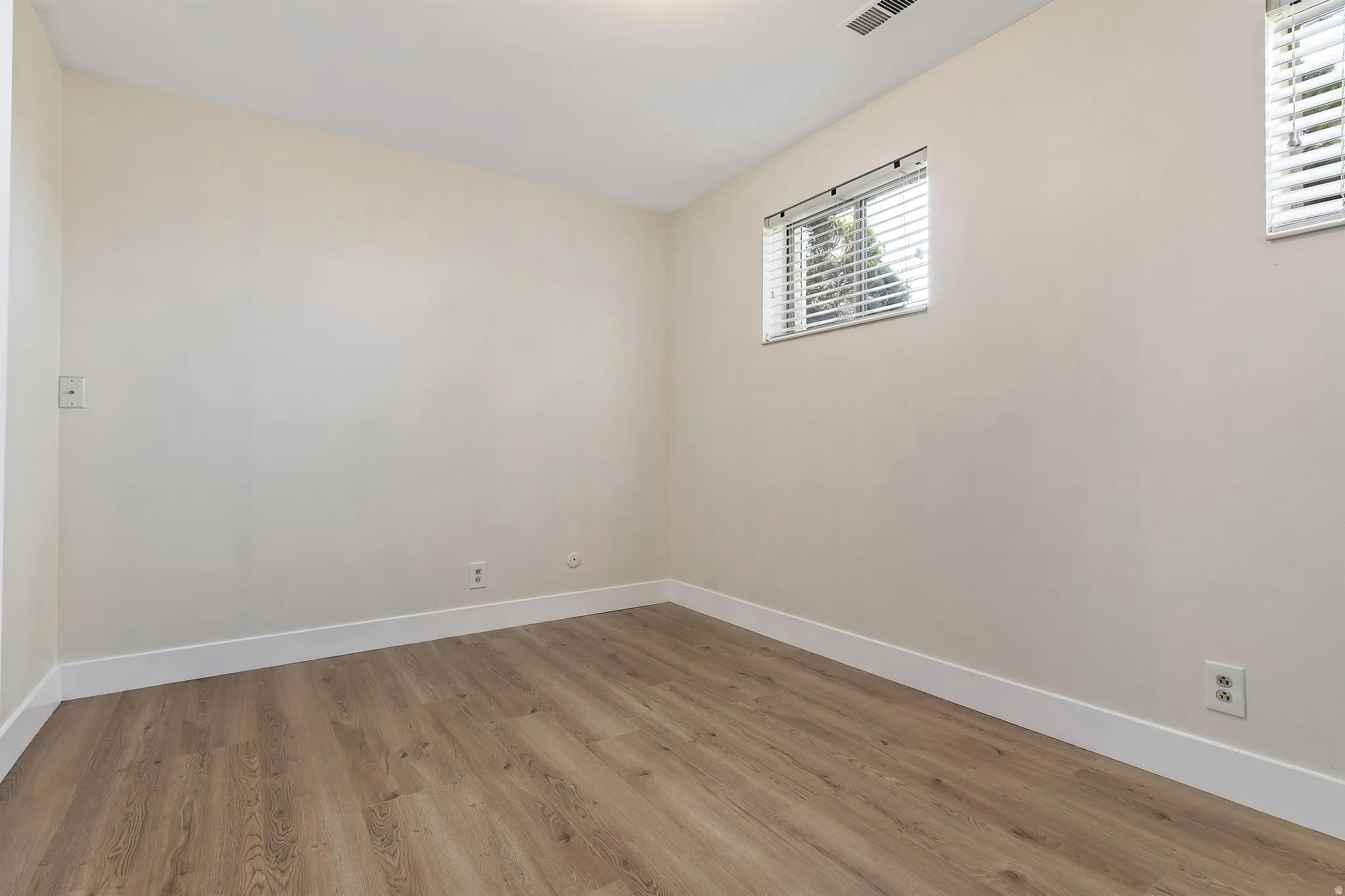 Room featuring light-toned walls, wood-finish flooring, white trim, and a window with horizontal blinds