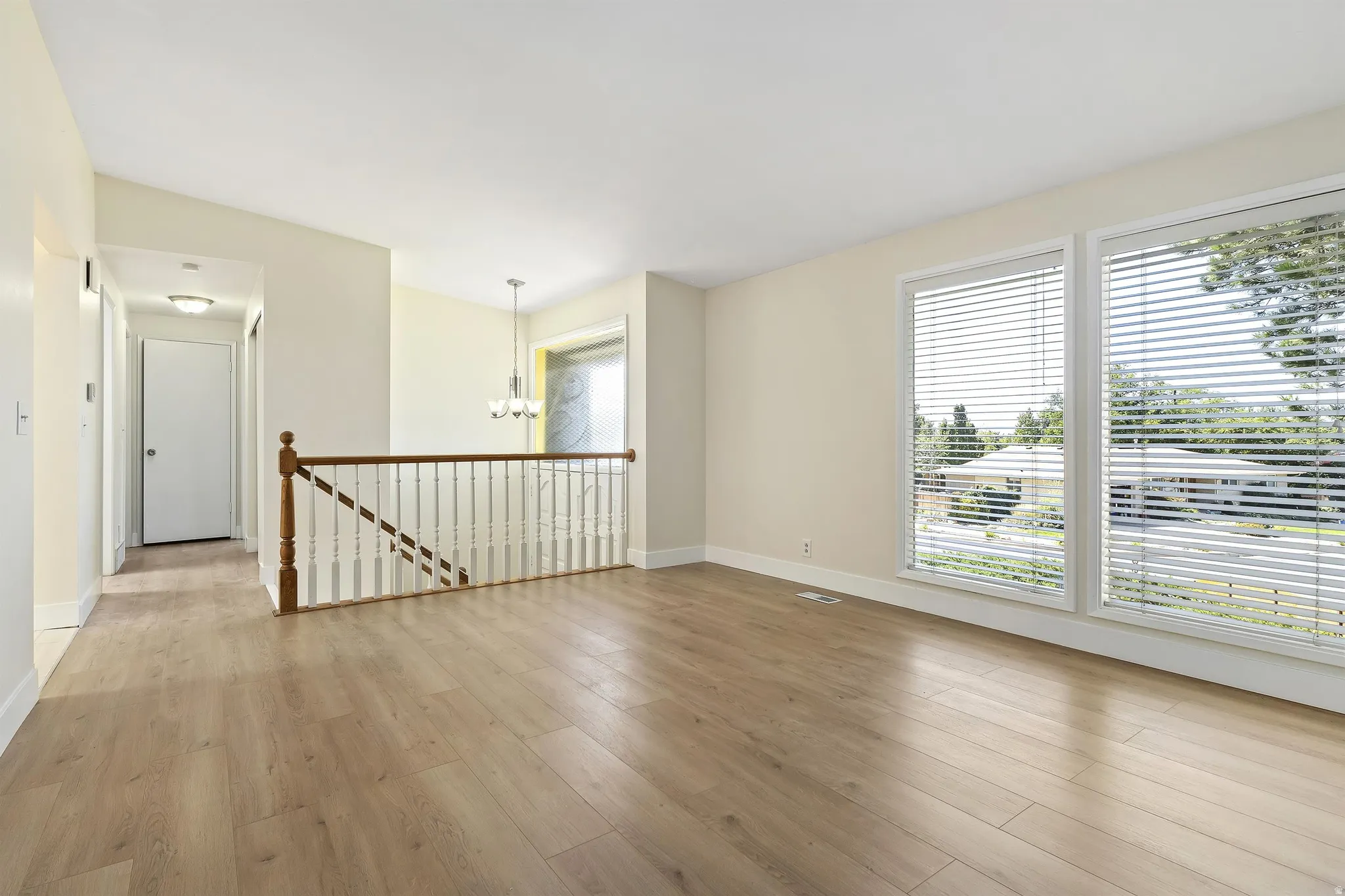 Wood-finish flooring, white trim, open staircase with wood handrail, dual windows with white blinds, and a neutral color palette