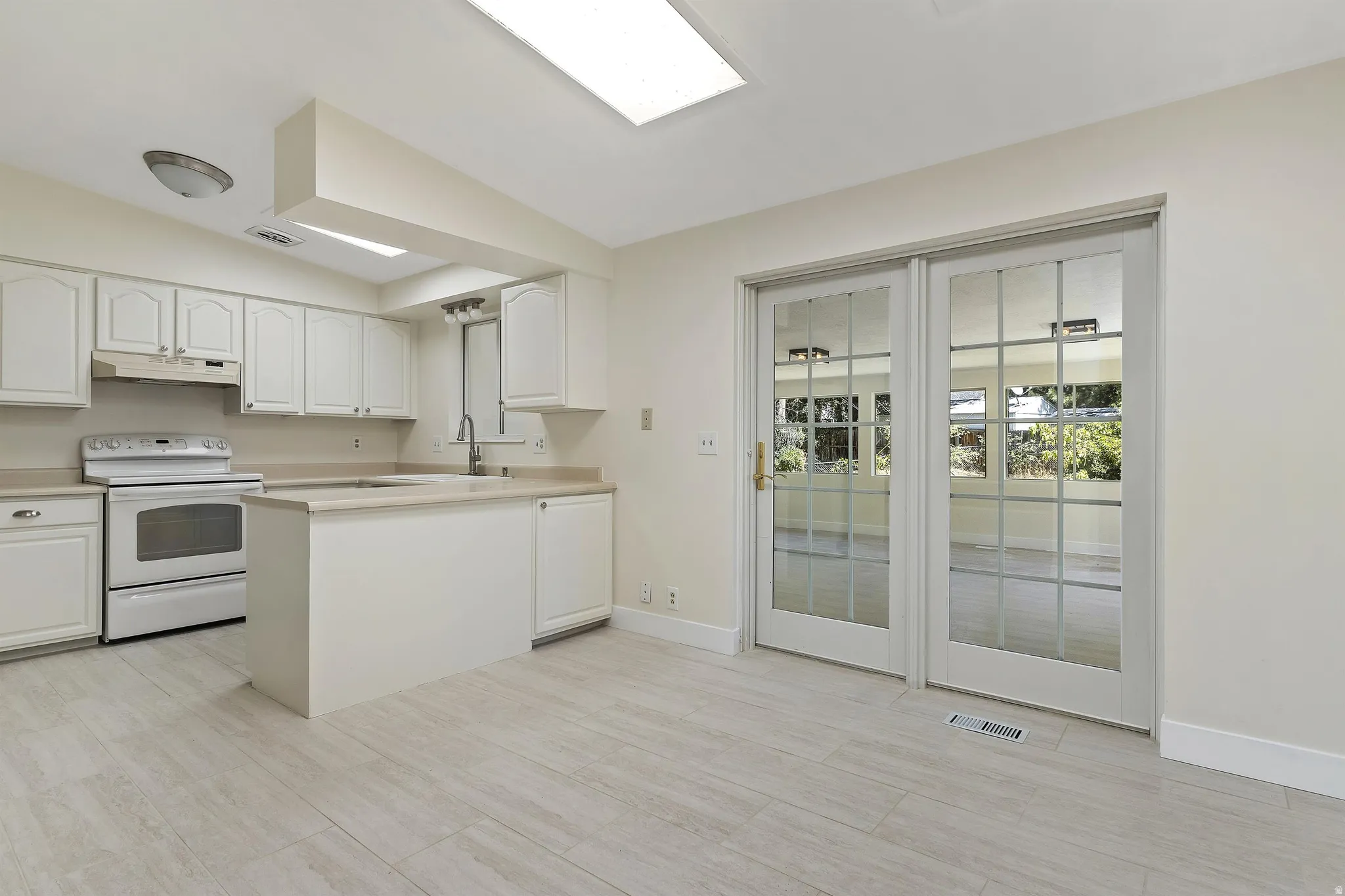 Kitchen featuring white cabinetry, a built-in island with a sink, white appliances, and wood-finish flooring