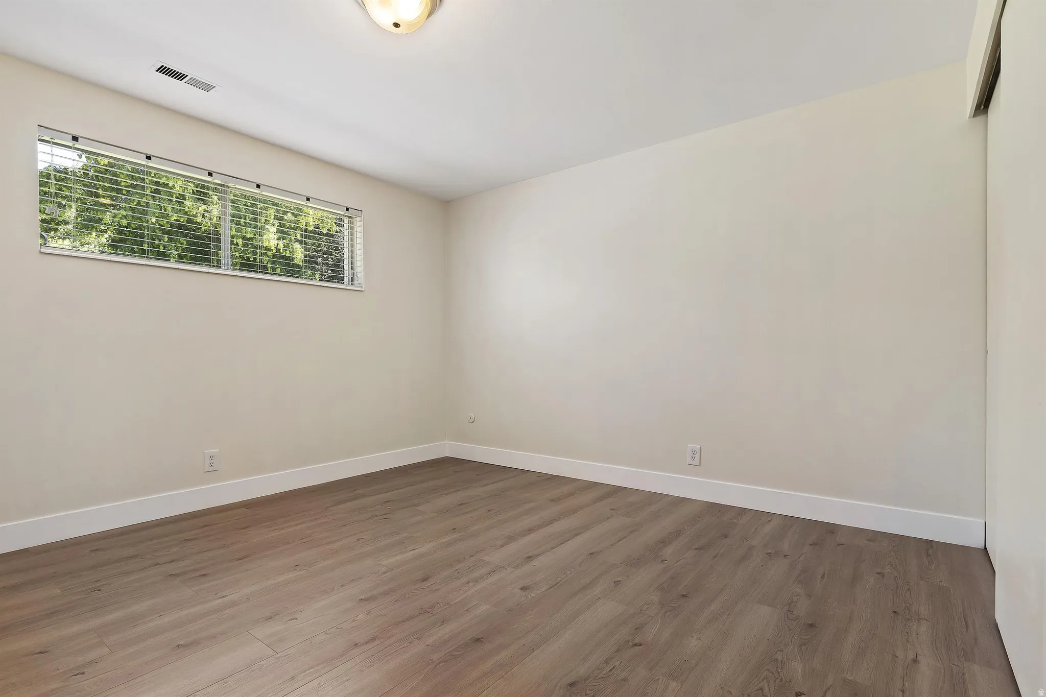 Wood-finish flooring, neutral wall tones, horizontal window with blinds, and flush-mount ceiling light