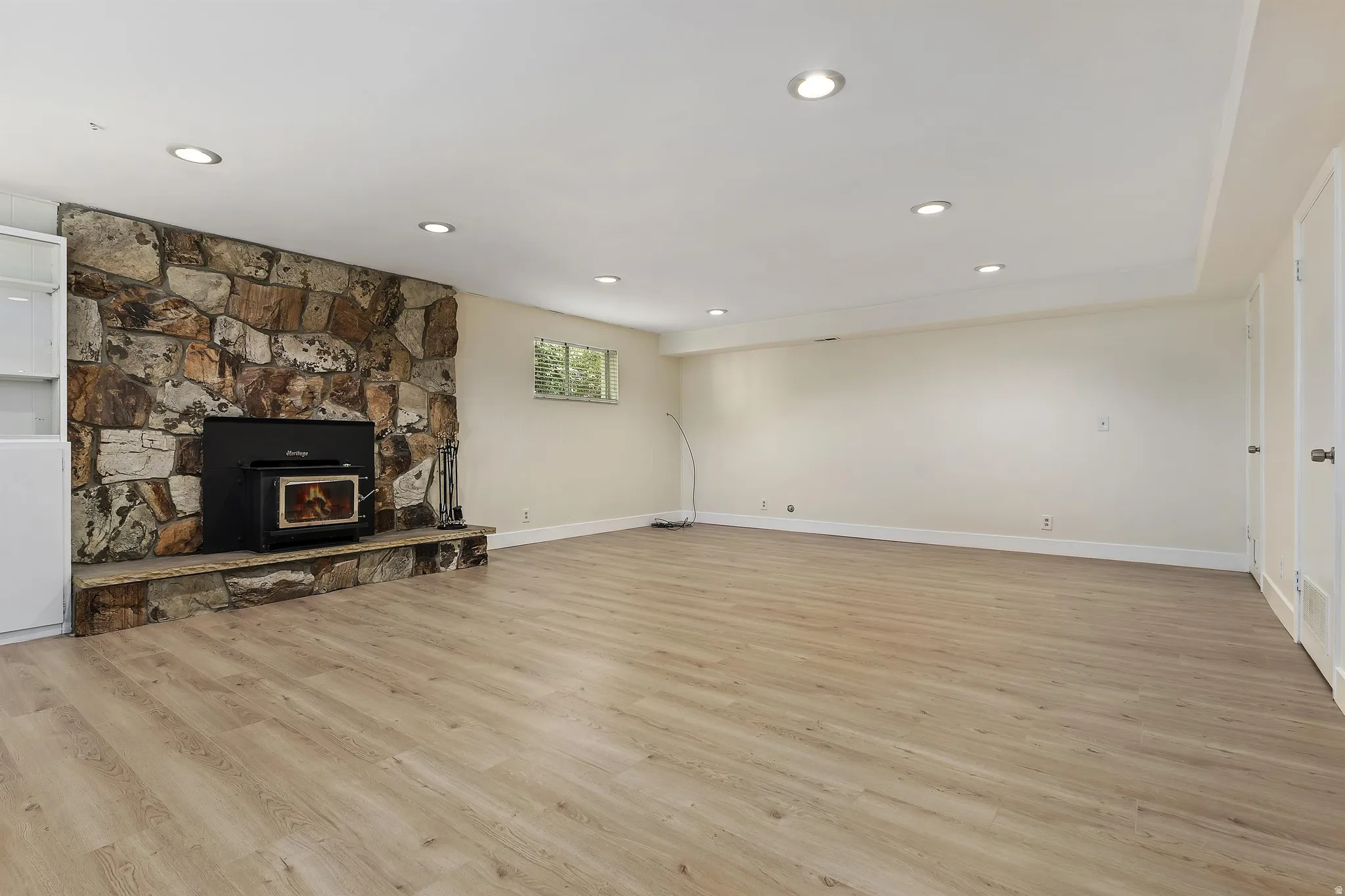 Stone veneer fireplace with an inset wood stove, wood-finish flooring, recessed lighting, and built-in white cabinetry
