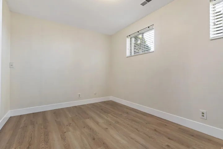Room featuring light-toned walls, wood-finish flooring, white trim, and a window with horizontal blinds