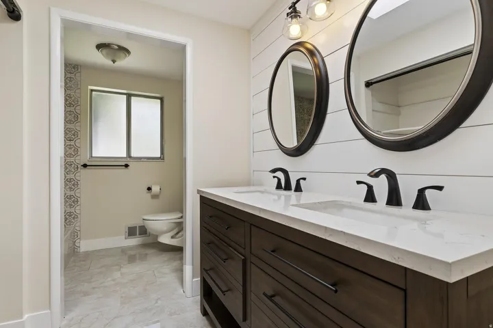 Dual vanity with a white countertop and integrated sinks, matte black fixtures, and wood-finish cabinetry