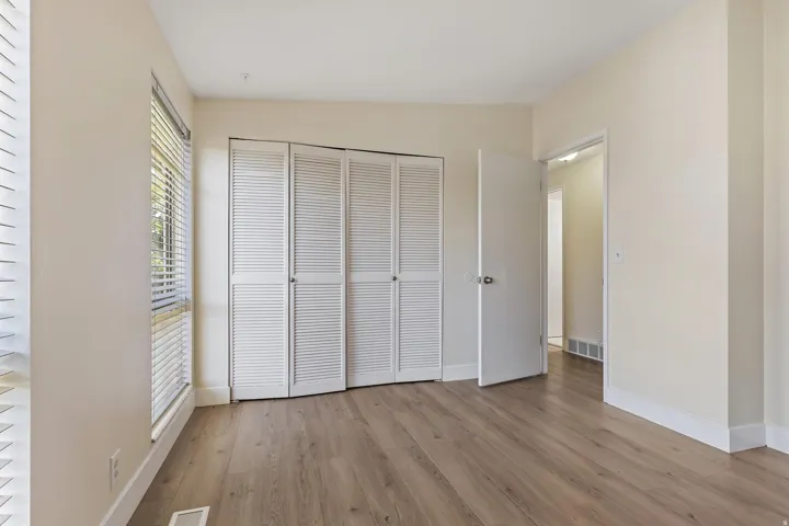 Wood-finish flooring, white louvered bifold closet doors, and neutral wall paint