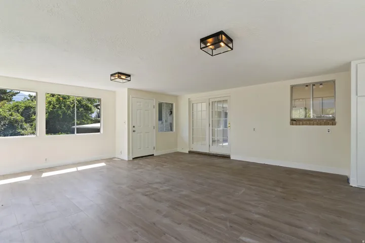 Spacious room featuring wood-finish flooring, multiple windows, a white paneled door, and white French doors