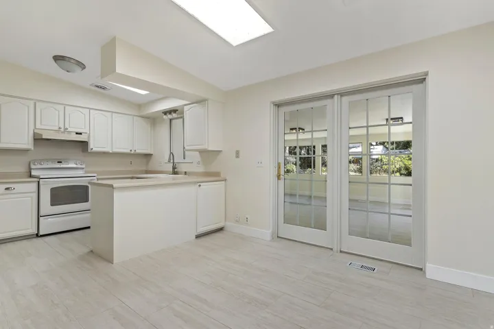 Kitchen featuring white cabinetry, a built-in island with a sink, white appliances, and wood-finish flooring