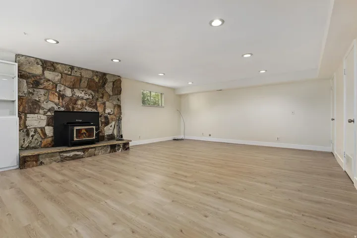 Stone veneer fireplace with an inset wood stove, wood-finish flooring, recessed lighting, and built-in white cabinetry