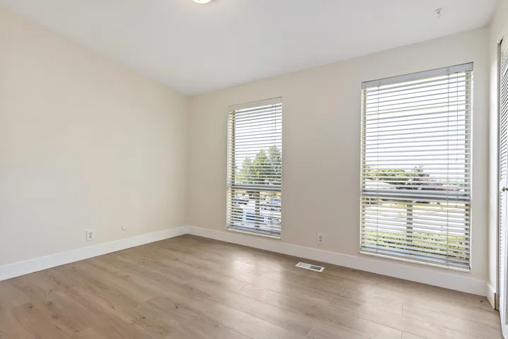 Wood-finish flooring with white baseboards, two large windows, and a flush-mounted ceiling light