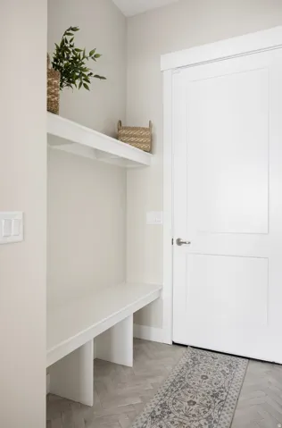 Built-in entryway bench, integrated shelving, bright white door, brushed nickel hardware, and herringbone-patterned flooring