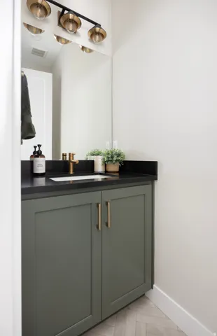 Vanity with green cabinetry, black countertop, and integrated sink