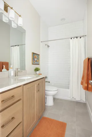 Light wood-finish vanity with gold-tone hardware, white countertop, and integrated rectangular sink