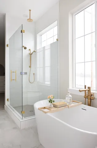 Spa-inspired primary bathroom featuring a freestanding soaking tub, walk-in shower enclosure with subway tile surround and brass fixtures, floating vanity with integrated sink, brass-accented pendant lighting, and abundant natural light from large multi-p