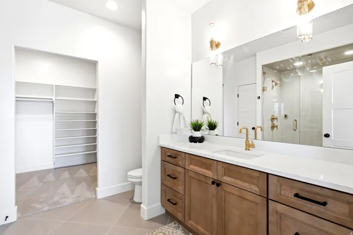 Dual-sink vanity with wood-finish cabinetry, white countertop, and gold-finish fixtures