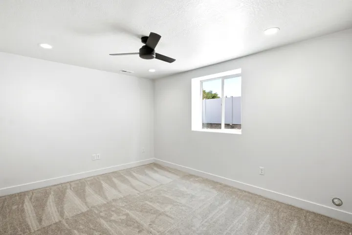 Recessed ceiling lighting, ceiling fan with black finish, white wall paint, patterned carpet flooring, and a window with white framing