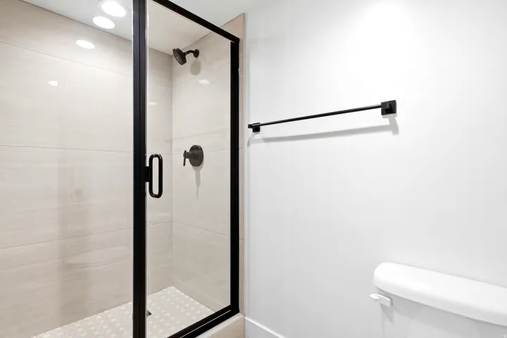 Glass-enclosed shower with matte black fixtures, light-toned wall tile, and a patterned shower pan