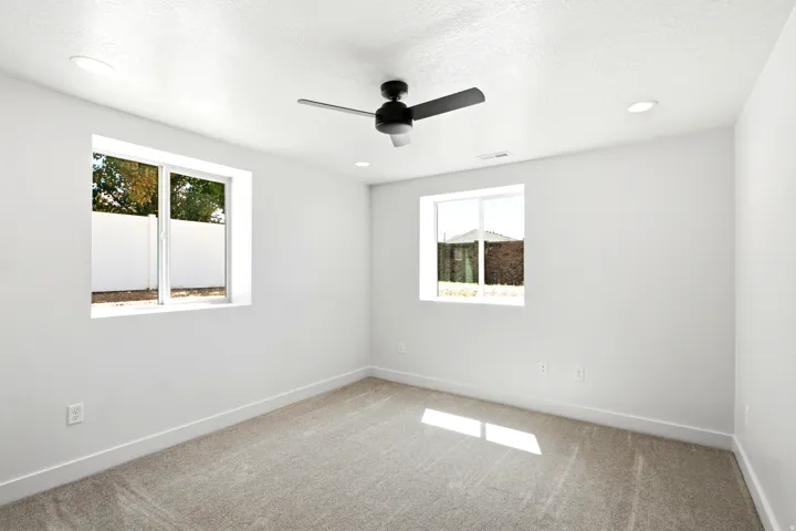Neutral tone wall paint, two windows, recessed lighting, ceiling fan, and carpeted flooring