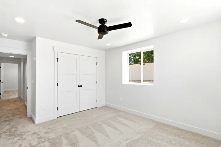 Recessed lighting, ceiling fan, neutral carpet, white paneled closet doors, and a window providing natural illumination