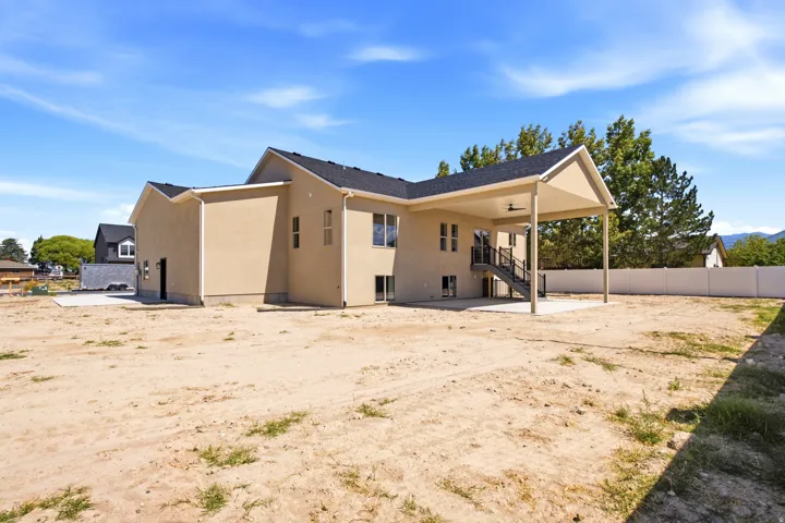 Stucco exterior with a covered patio, concrete pad, exterior staircase, and a dark shingle roof