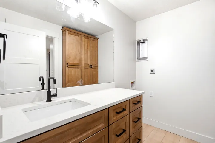 Expansive vanity with a white rectangular undermount sink, matte black faucet, and light wood-finish cabinetry