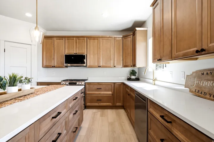Kitchen featuring extensive wood cabinetry, white countertops, stainless steel appliances, a center island with storage, and wood-finish flooring