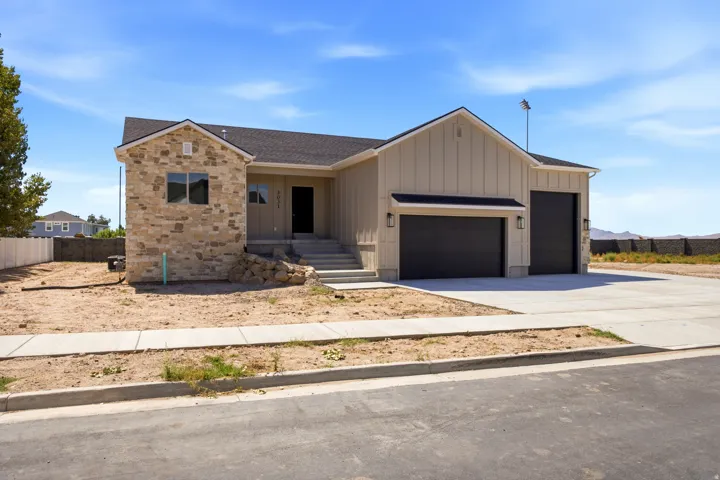 Stone veneer facade with vertical siding accents, dark roof, dark garage doors, concrete driveway, and concrete sidewalk
